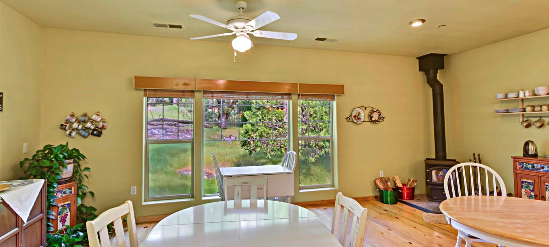 A yellow walled dining room with white wooden tables and chairs with a wood burning stove in the corner. 